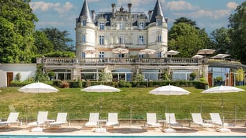 Un grand bâtiment historique doté d’une piscine, d’un espace extérieur aménagé et de parasols.