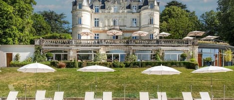 A large, historic building with a swimming pool, outdoor seating, and umbrellas.