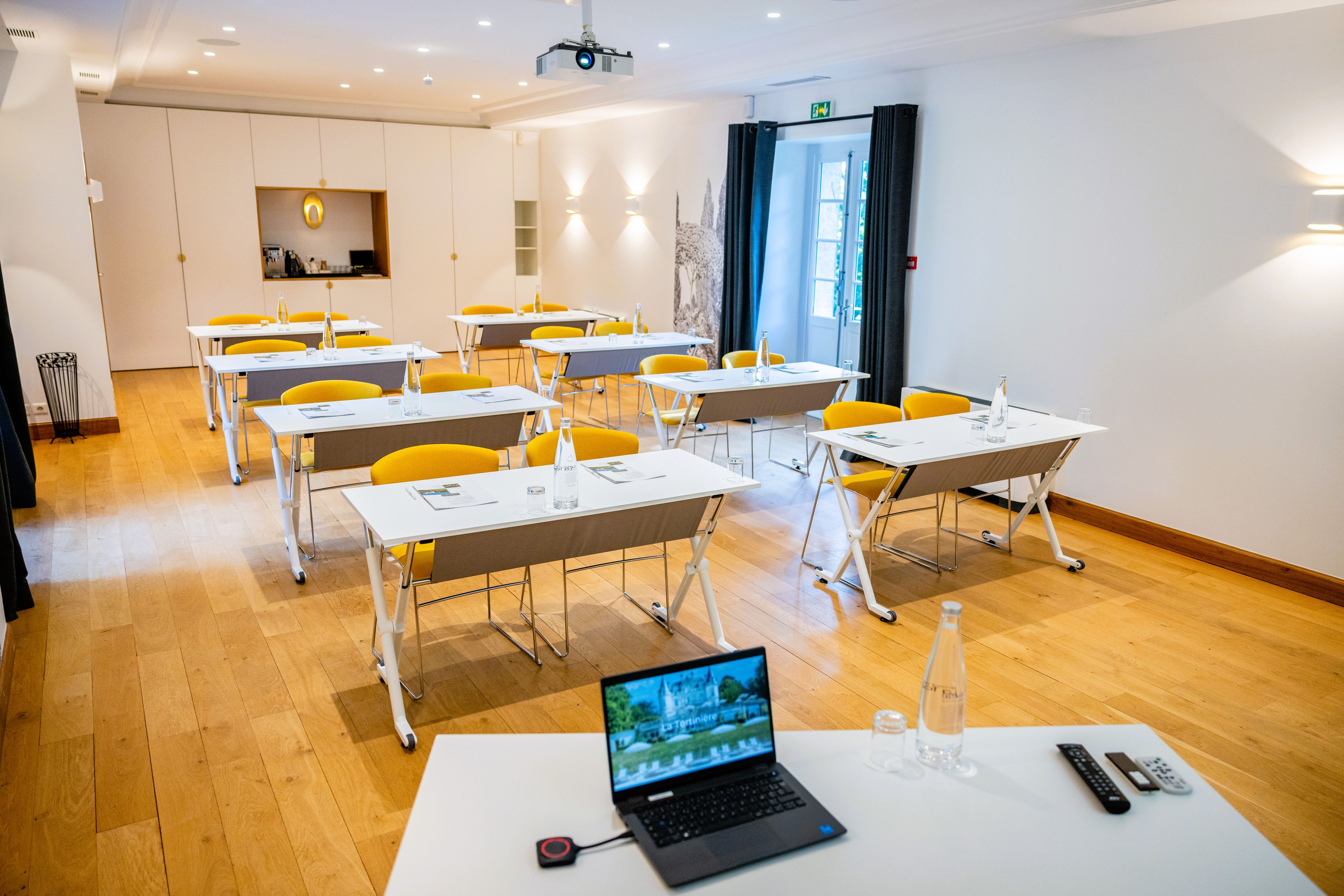 Una sala de conferencias con mesas, sillas, una computadora portátil y un proyector.