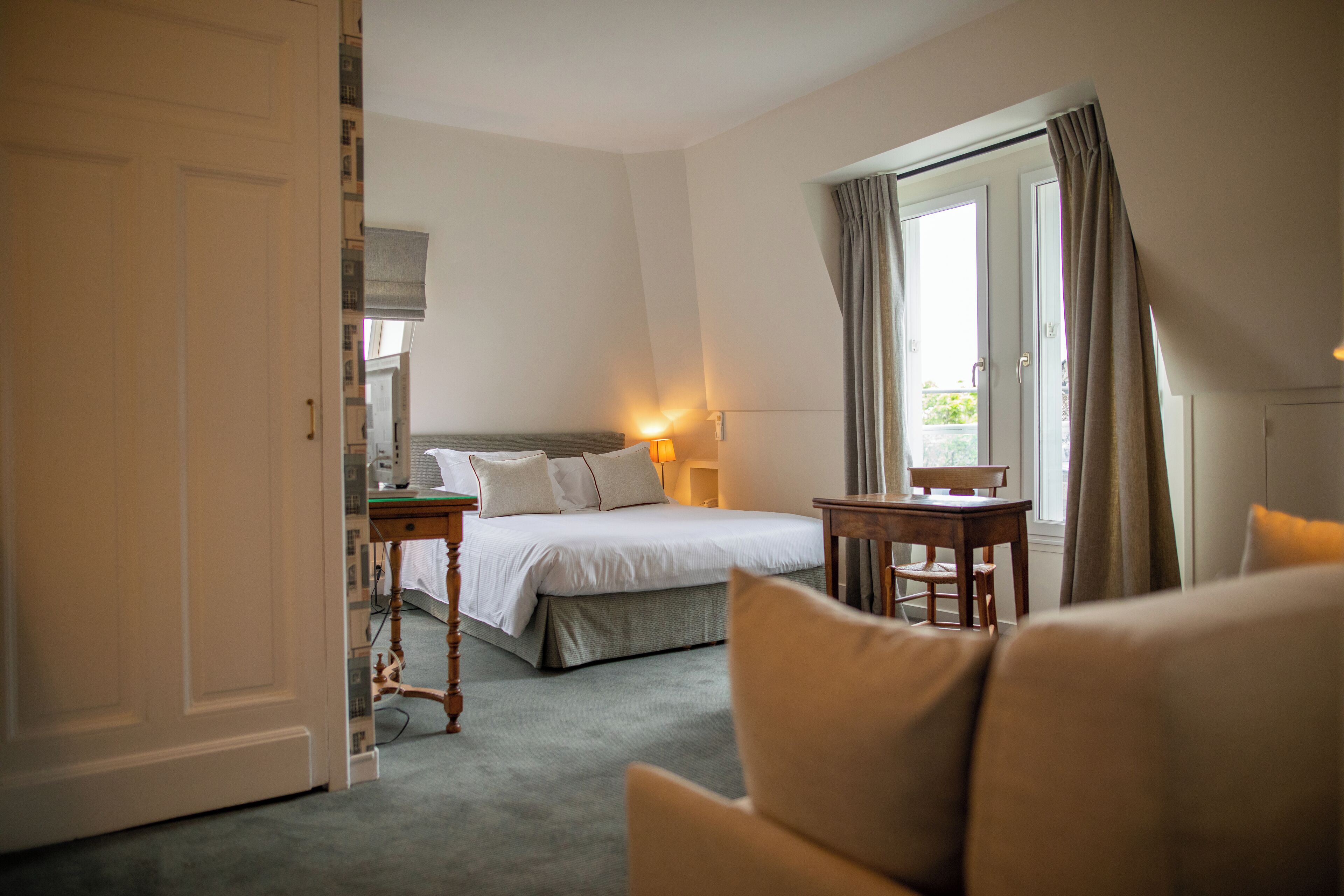 A hotel room with a bed, a desk, a chair, and a window with curtains.
