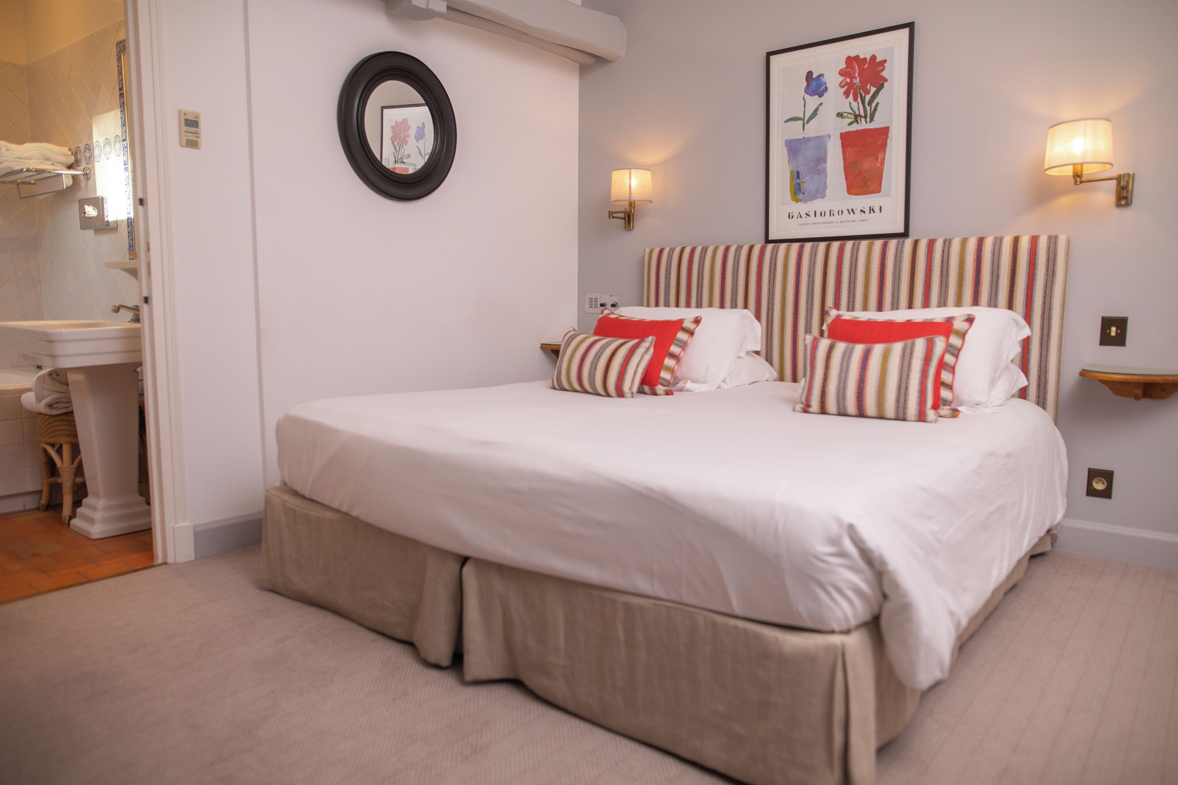 A bedroom with a large bed, a bedside table, a mirror, and a wall-mounted light fixture.