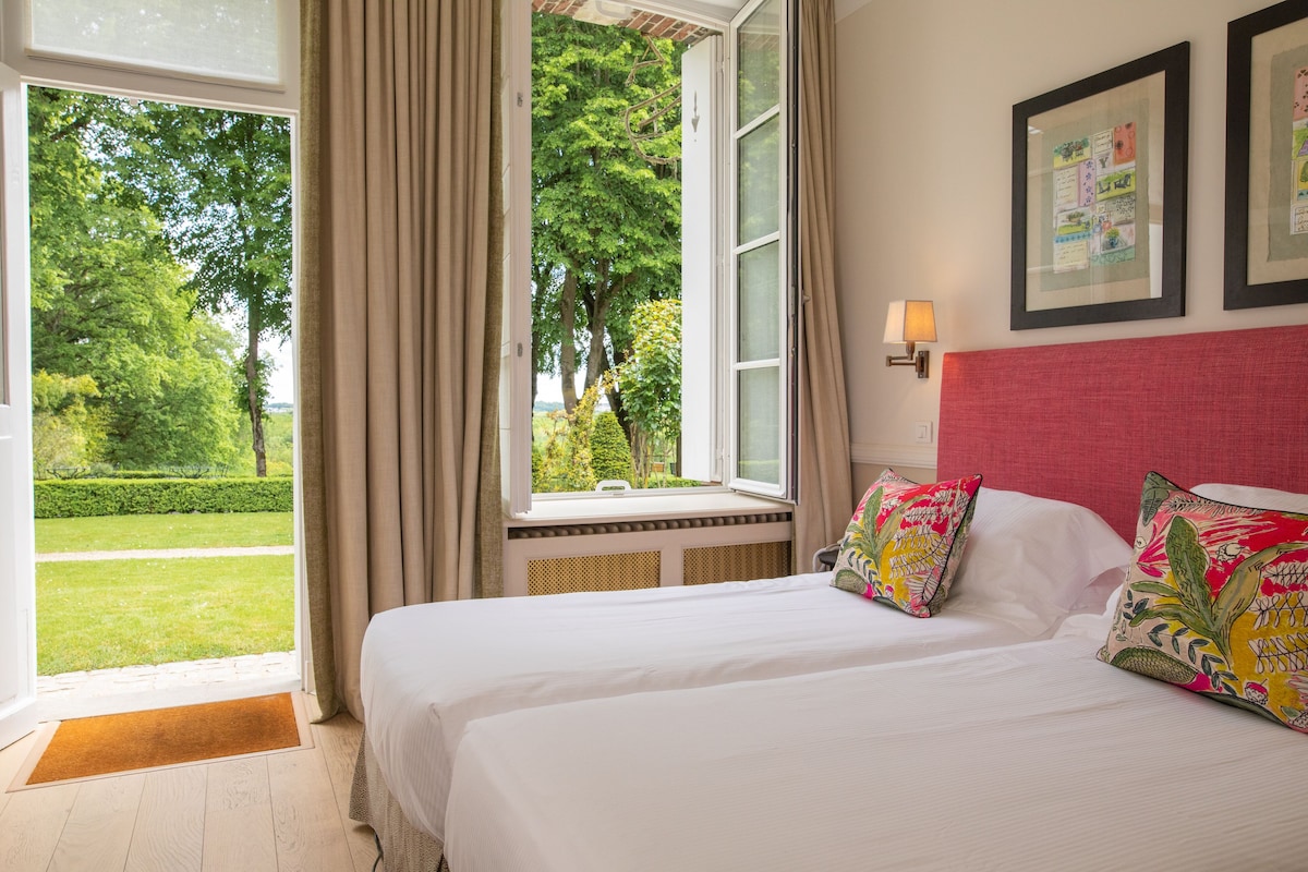 A hotel room with a large bed, a window with curtains, a red headboard, and framed pictures on the wall.