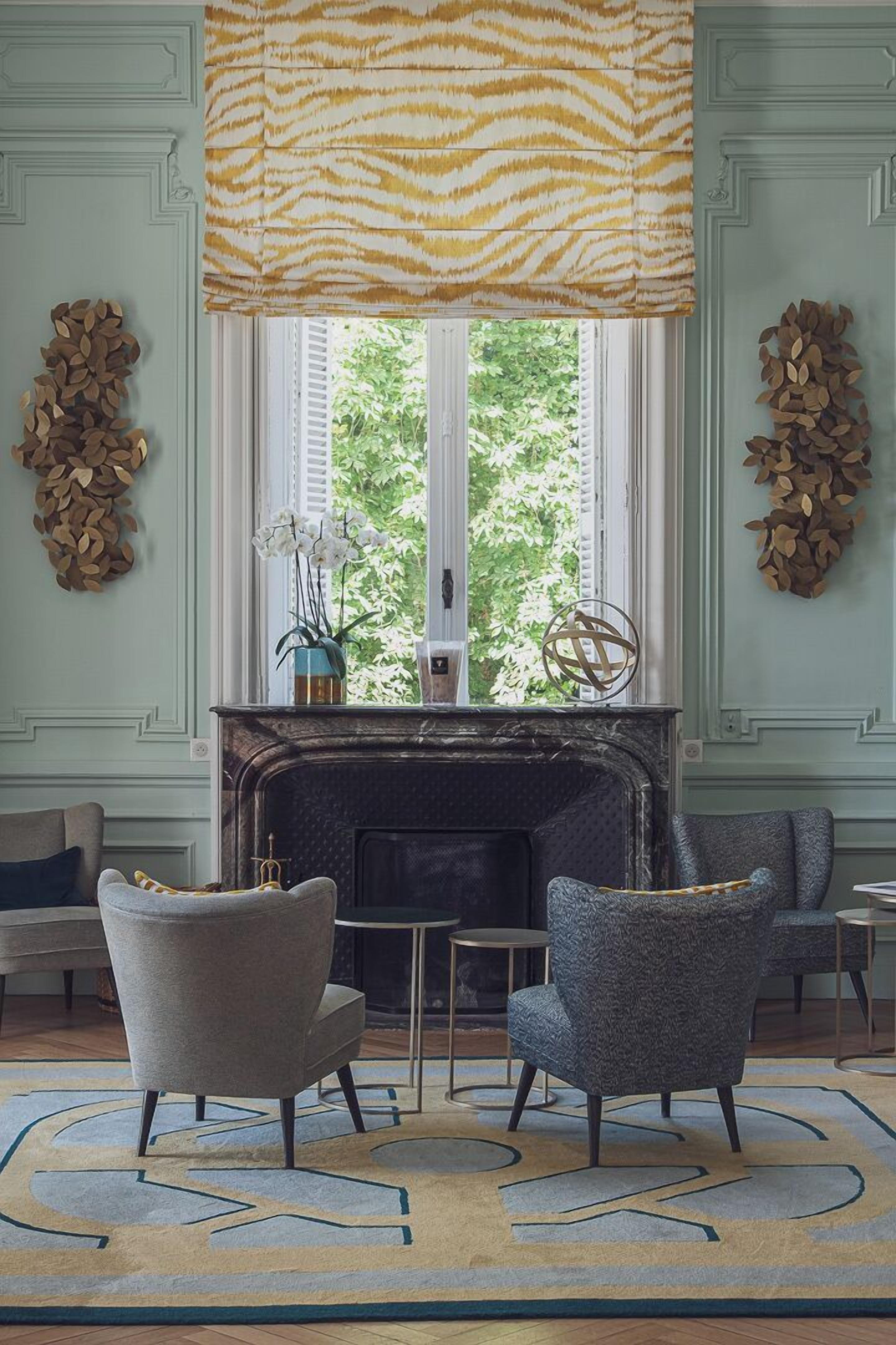A room with a fireplace, two armchairs, a table, and a window with a zebra-striped blind.