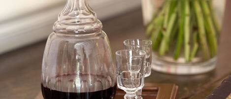 A decanter of red wine on a tray with two glasses, a vase of flowers, and a book on a wooden table.