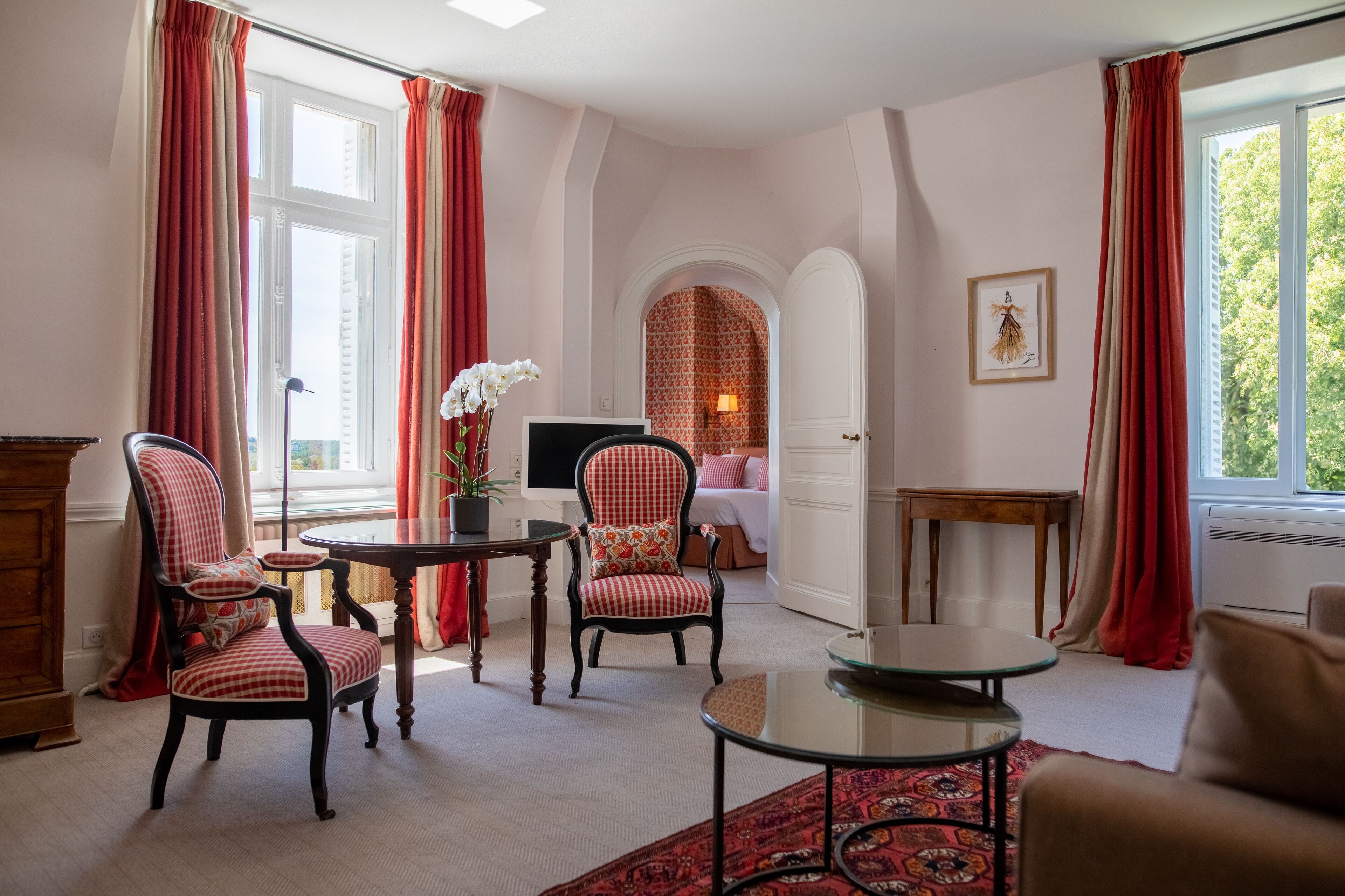 Una habitación con dos sillones, una mesita, un sofá y un ventanal con cortinas rojas.