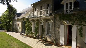 A two-story house with a balcony, a paved driveway, and outdoor seating.