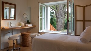 Une chambre avec une grande fenêtre, un bureau en bois, une chaise, un lit et un miroir.