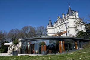 Un edificio imponente con una extensión moderna de vidrio, que presenta un comedor con sillas y mesas, y un gran árbol en primer plano.