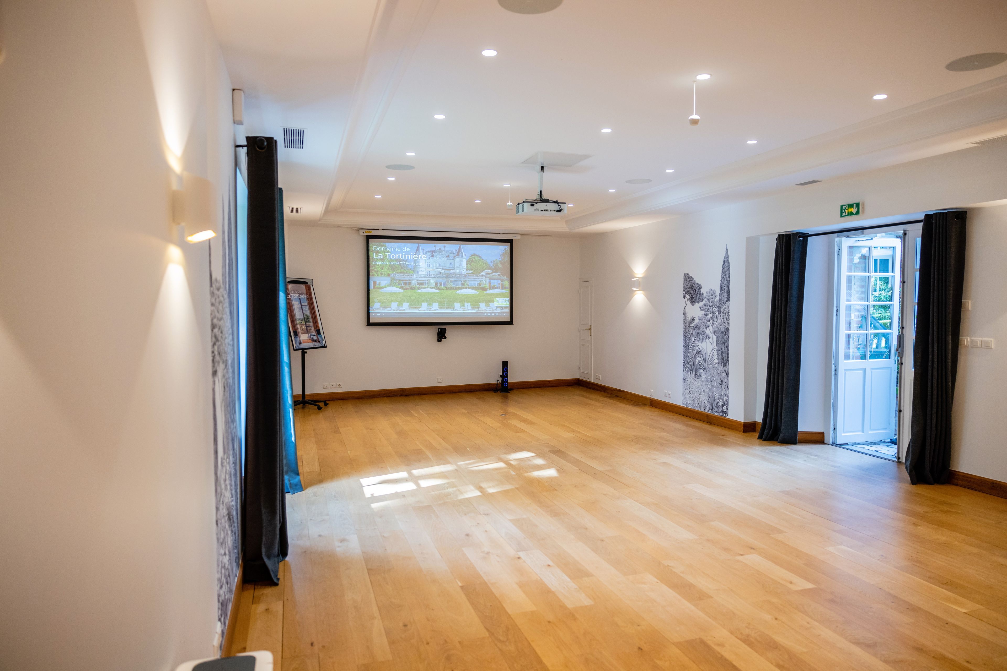 A spacious room with a wooden floor, a projection screen, and a door leading outside.