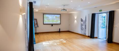A spacious room with a wooden floor, a projection screen, and a door leading outside.