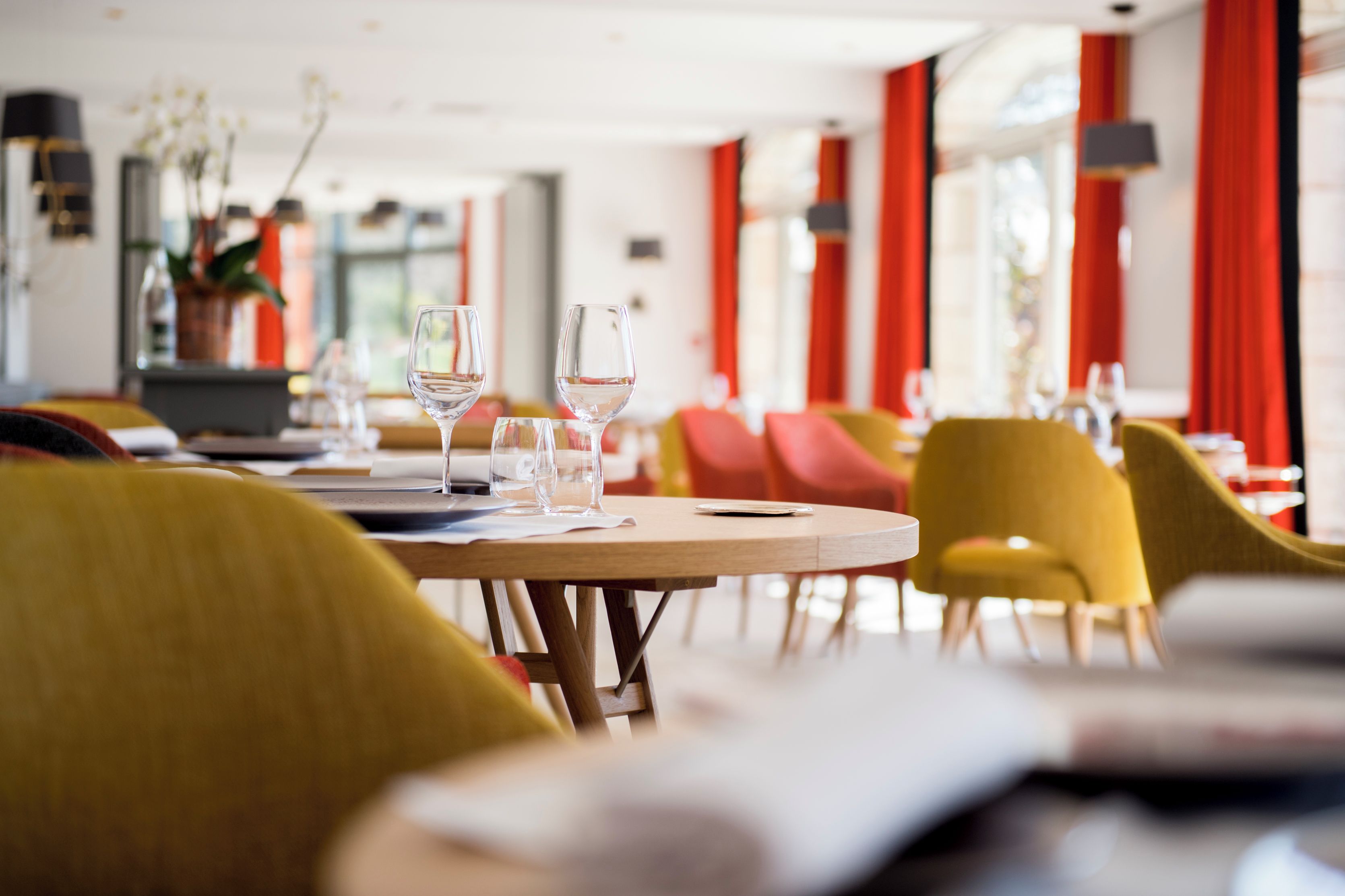 A restaurant interior with round tables, chairs, and empty wine glasses.