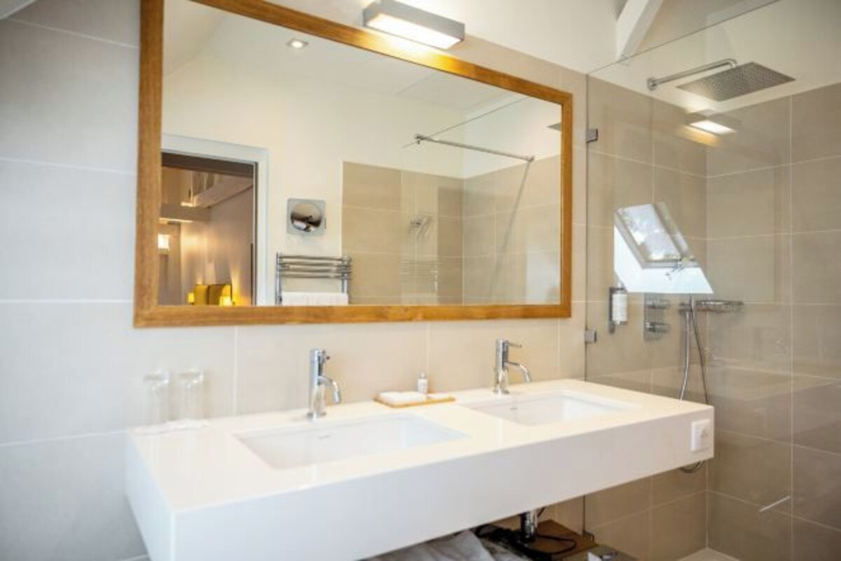 Une salle de bain moderne avec deux lavabos, un grand miroir et un espace douche.