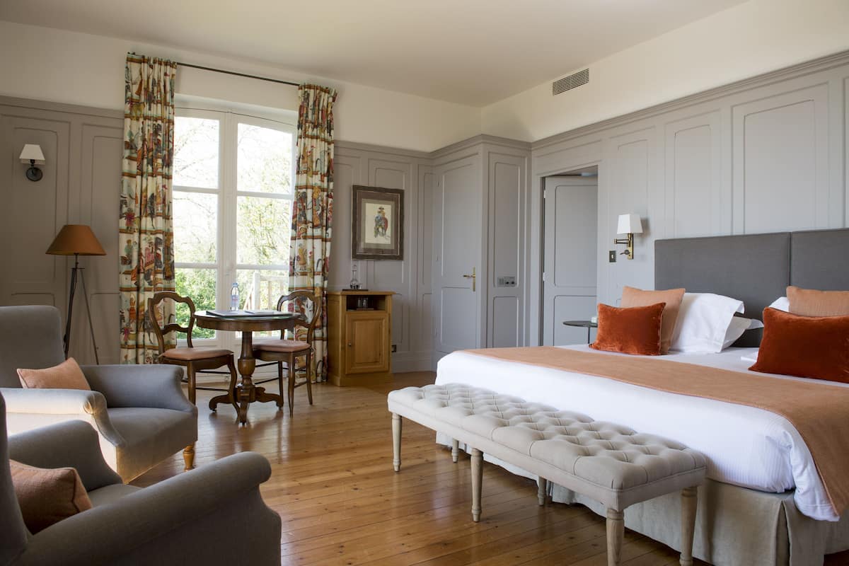 A bedroom with a large bed, a bench, a chair, a table, and a desk.
