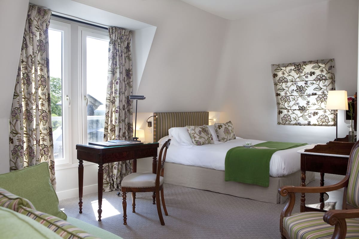 A hotel room with a bed, a desk, a chair, and a window with curtains.