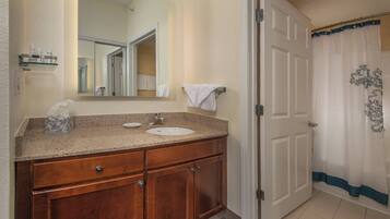 A bathroom with a wooden vanity, a sink, a mirror, and a door with a curtain.