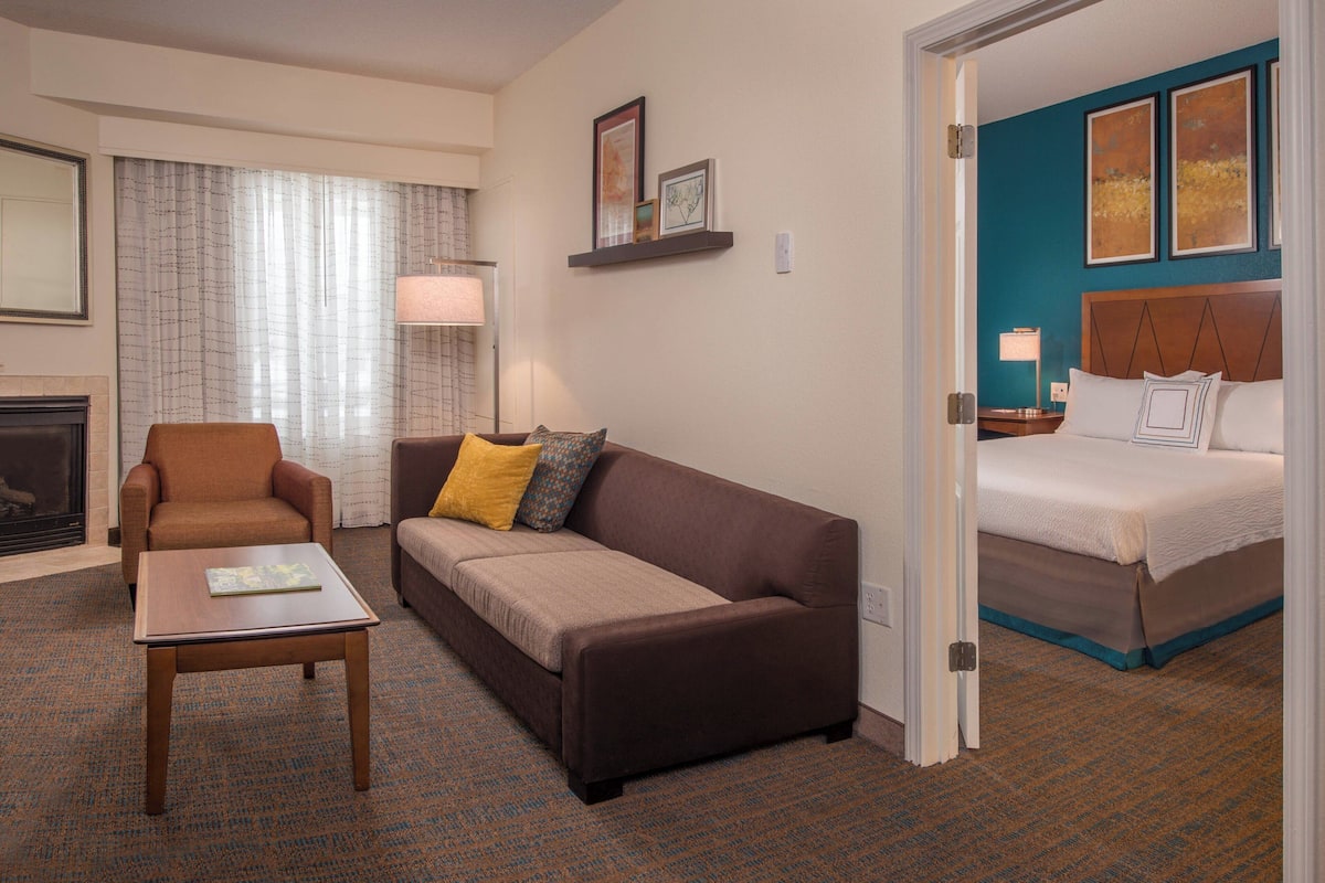 Una habitación de hotel con un sofá marrón, una mesita de madera, una cama con una pared de acento azul y una chimenea.