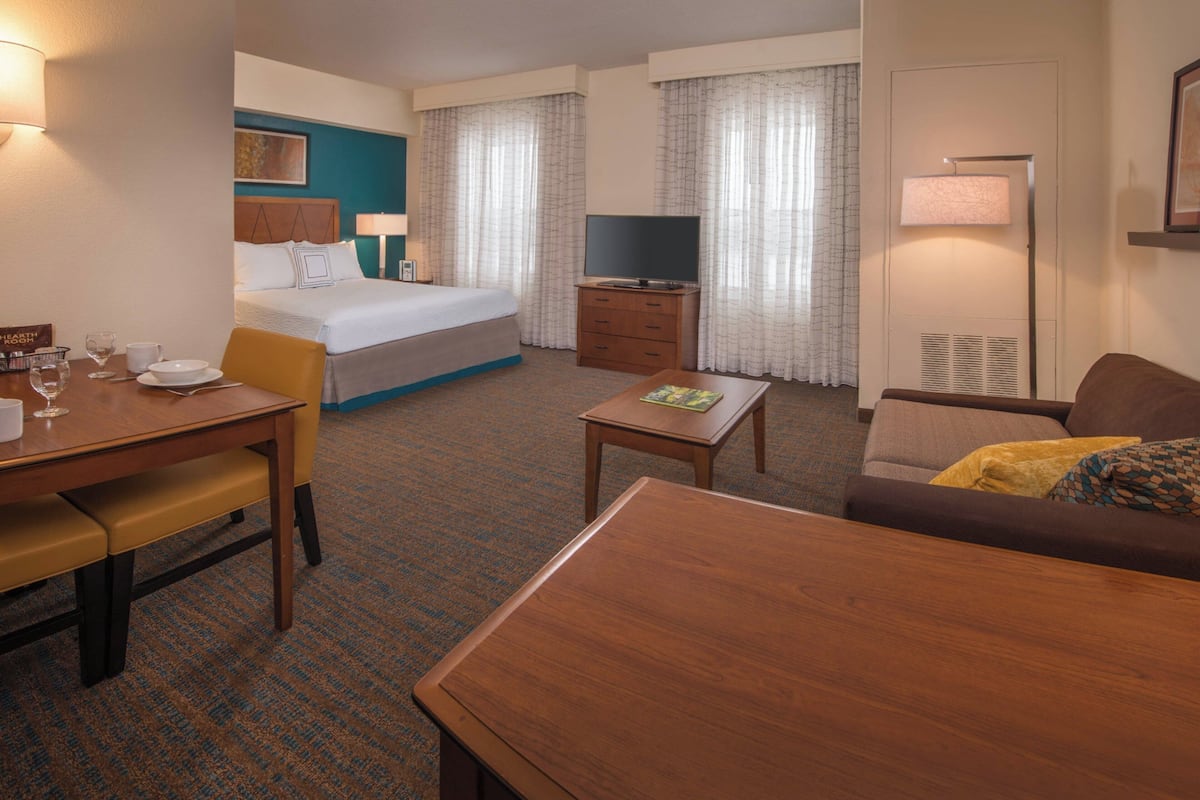Habitación de hotel con cama, televisión, escritorio con silla, sofá y lámpara.