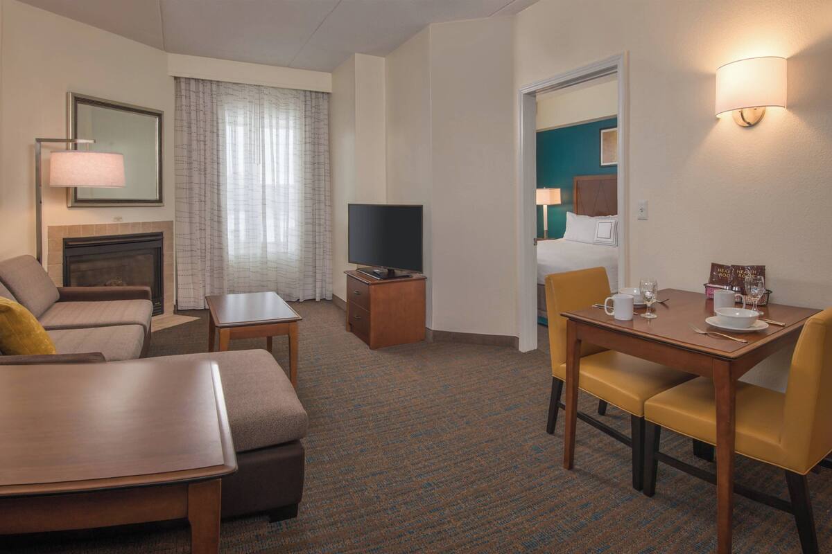 Habitación de hotel con sofá, una mesita, televisor, mesa de comedor con sillas y chimenea.