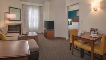 A hotel room with a sofa, a small table, a TV, a dining table with chairs, and a fireplace.