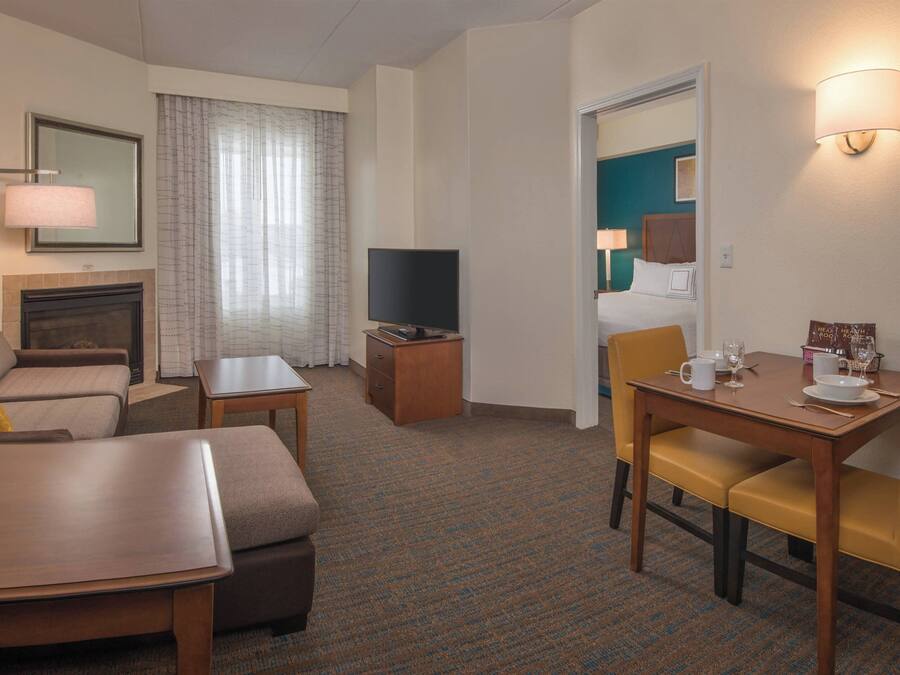 A hotel room with a sofa, a small table, a TV, a dining table with chairs, and a fireplace.