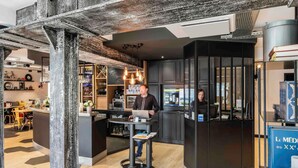 A modern interior with a bar area, a counter with a laptop, and a seating area with a wooden floor. - ibis Styles Dinan Centre Ville (Dinan)