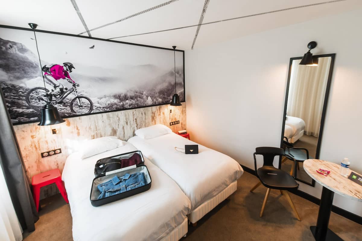 Hotelkamer met twee bedden, een bureau, een stoel, een spiegel en een muur met een schilderij van een mountainbike.