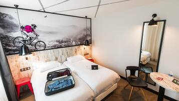 Hotelkamer met twee bedden, een bureau, een stoel, een spiegel en een muur met een schilderij van een mountainbike.