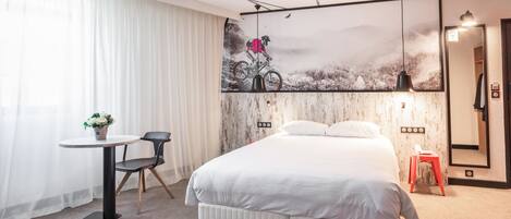 Una habitación de hotel moderna con una cama grande, una mesita con una silla, un escritorio y un espejo amplio.