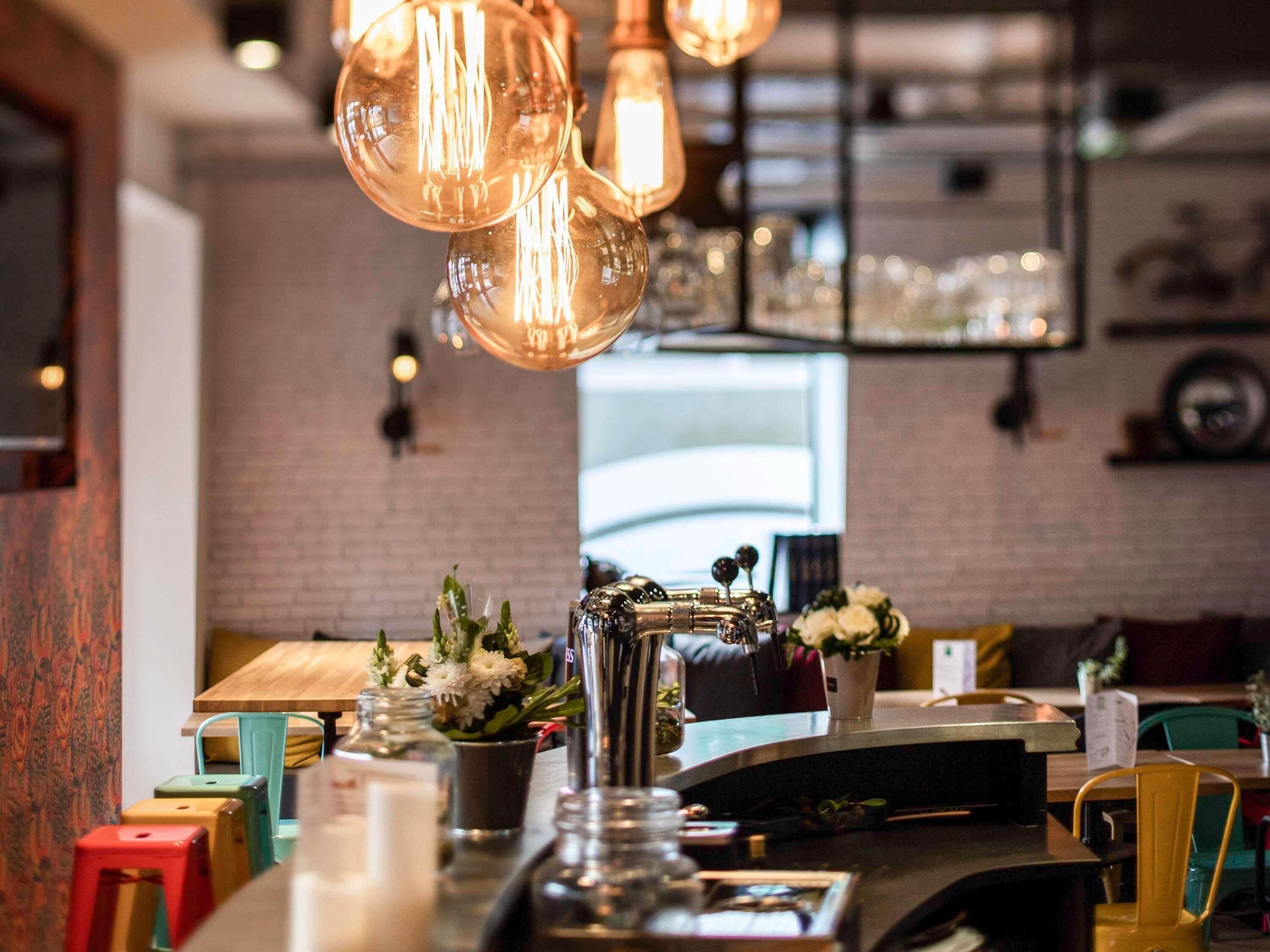 Zona de bar con pared de ladrillo, lámparas colgantes y una barra con diversos objetos.