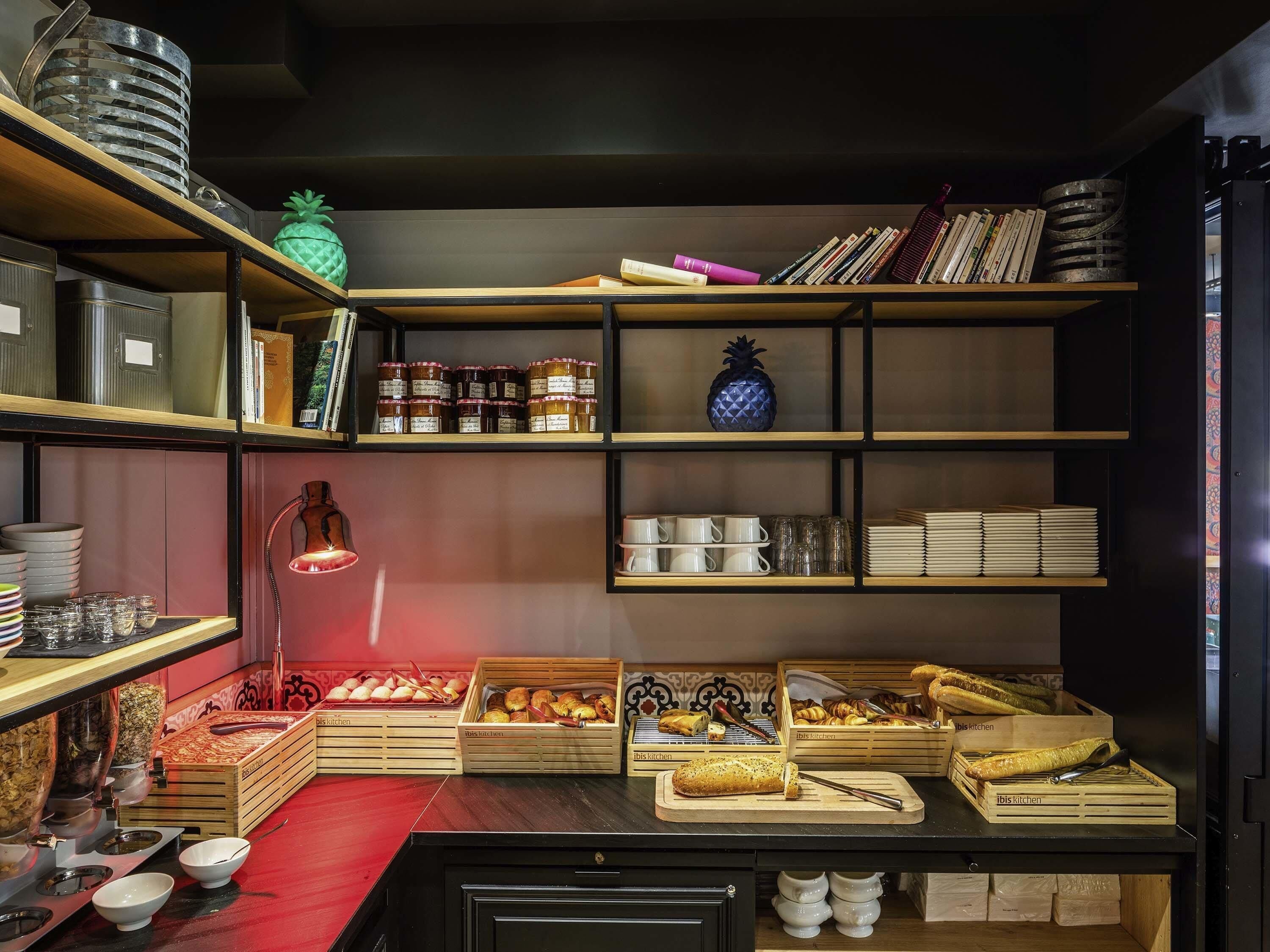 A kitchen area with shelves containing jars, books, and a pineapple. There are also bread baskets and a coffee machine.