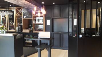 A modern bar area with a laptop on a table, shelves with glasses, and a chalkboard menu.