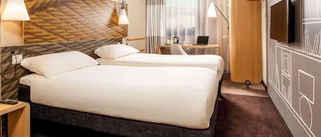 A hotel room with two beds, a desk with a laptop, a TV, and a patterned wall.