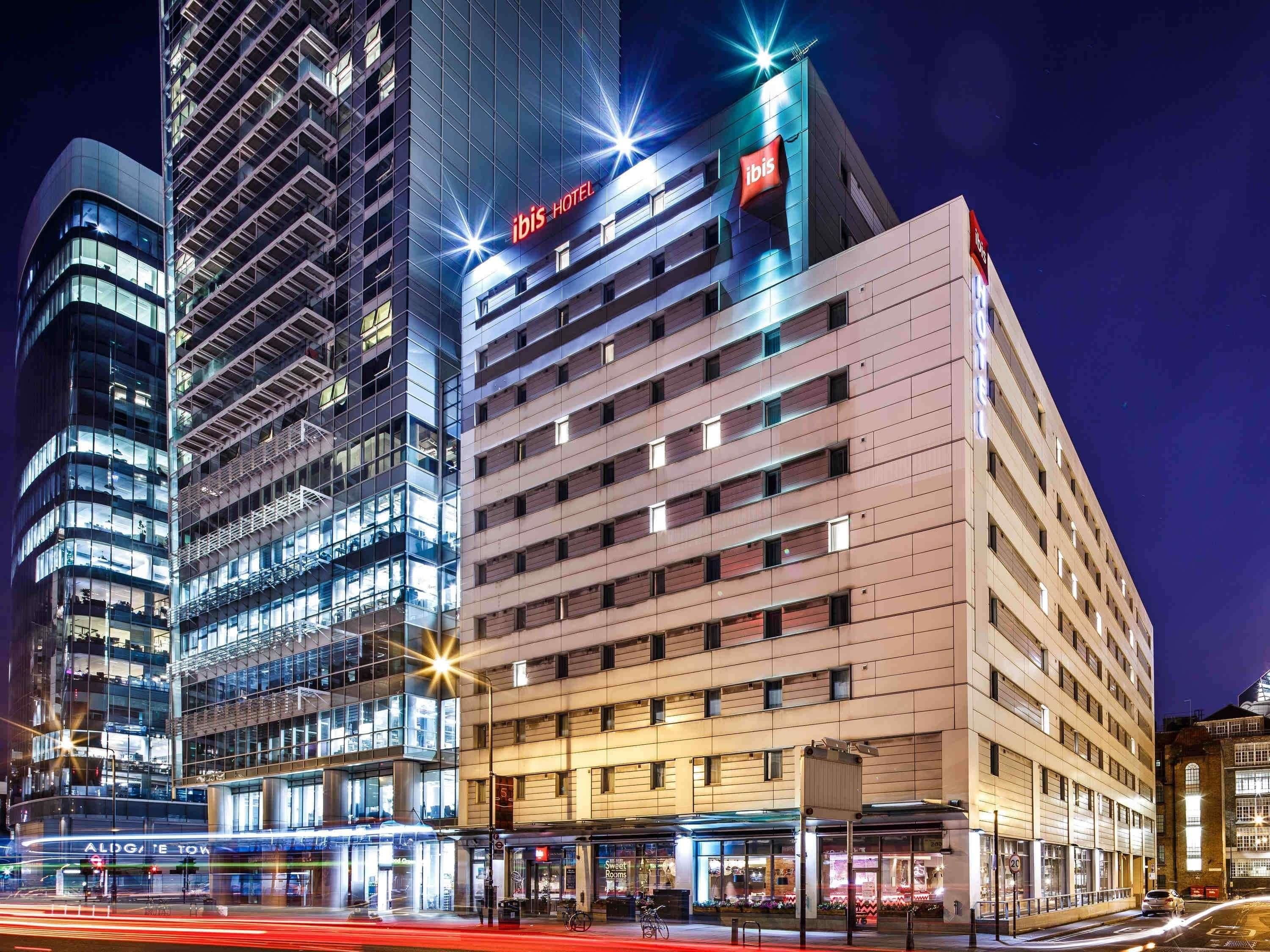A modern hotel with a prominent 'ibis HOTEL' sign, a glass facade, and a ground-level retail space.