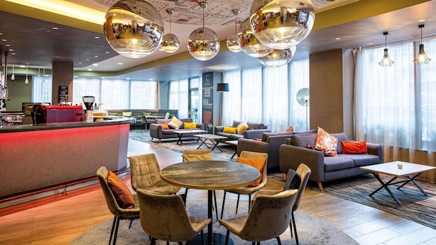 En modern hotellobby med ett runt matbord, soffor och en bardisk.