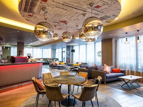 A modern hotel lobby with a round dining table, sofas, and a bar area.. ibis London City - Shoreditch