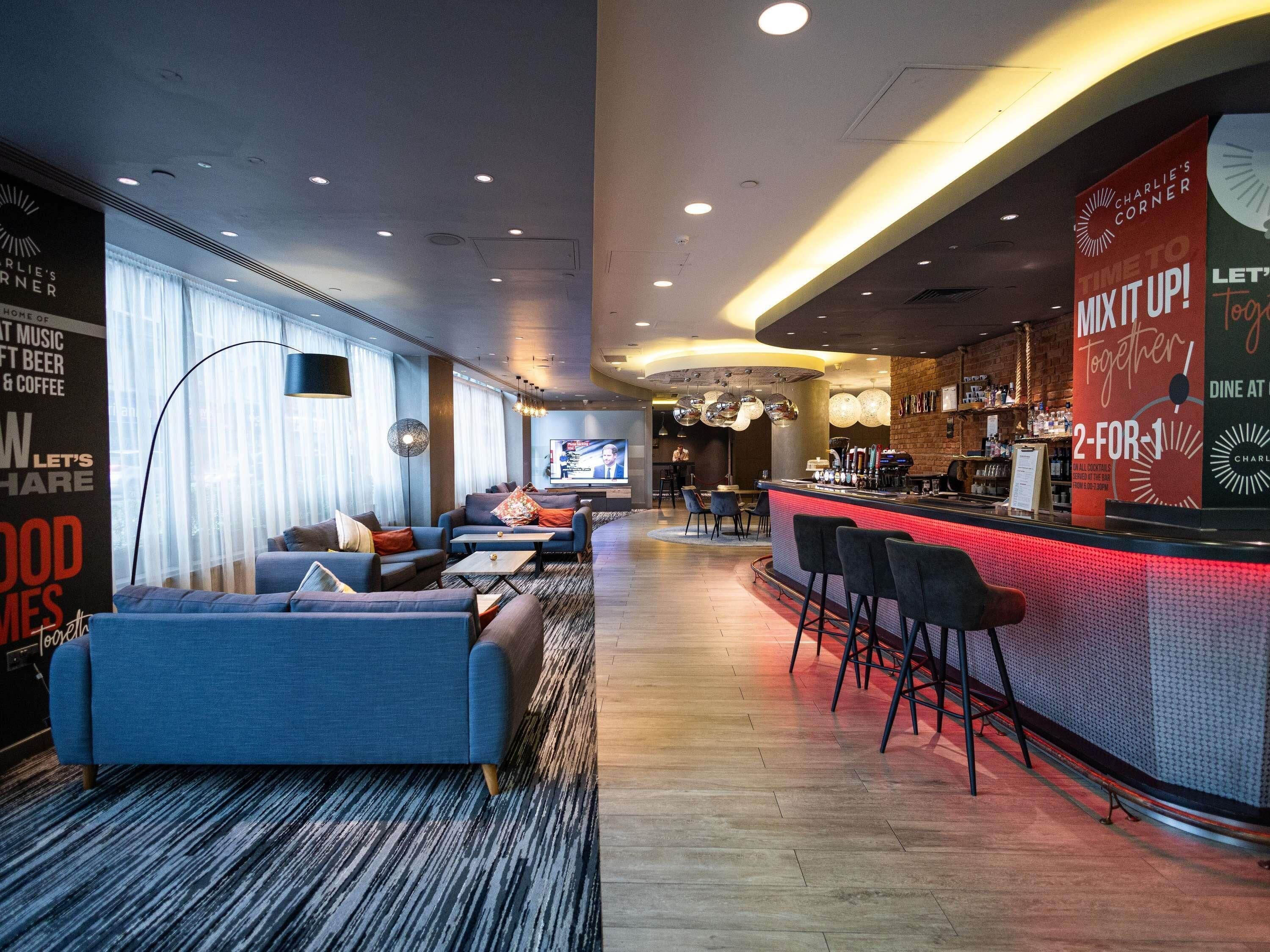 A modern bar area with a counter, bar stools, and a television screen. There are sofas and a coffee table in the seating area.