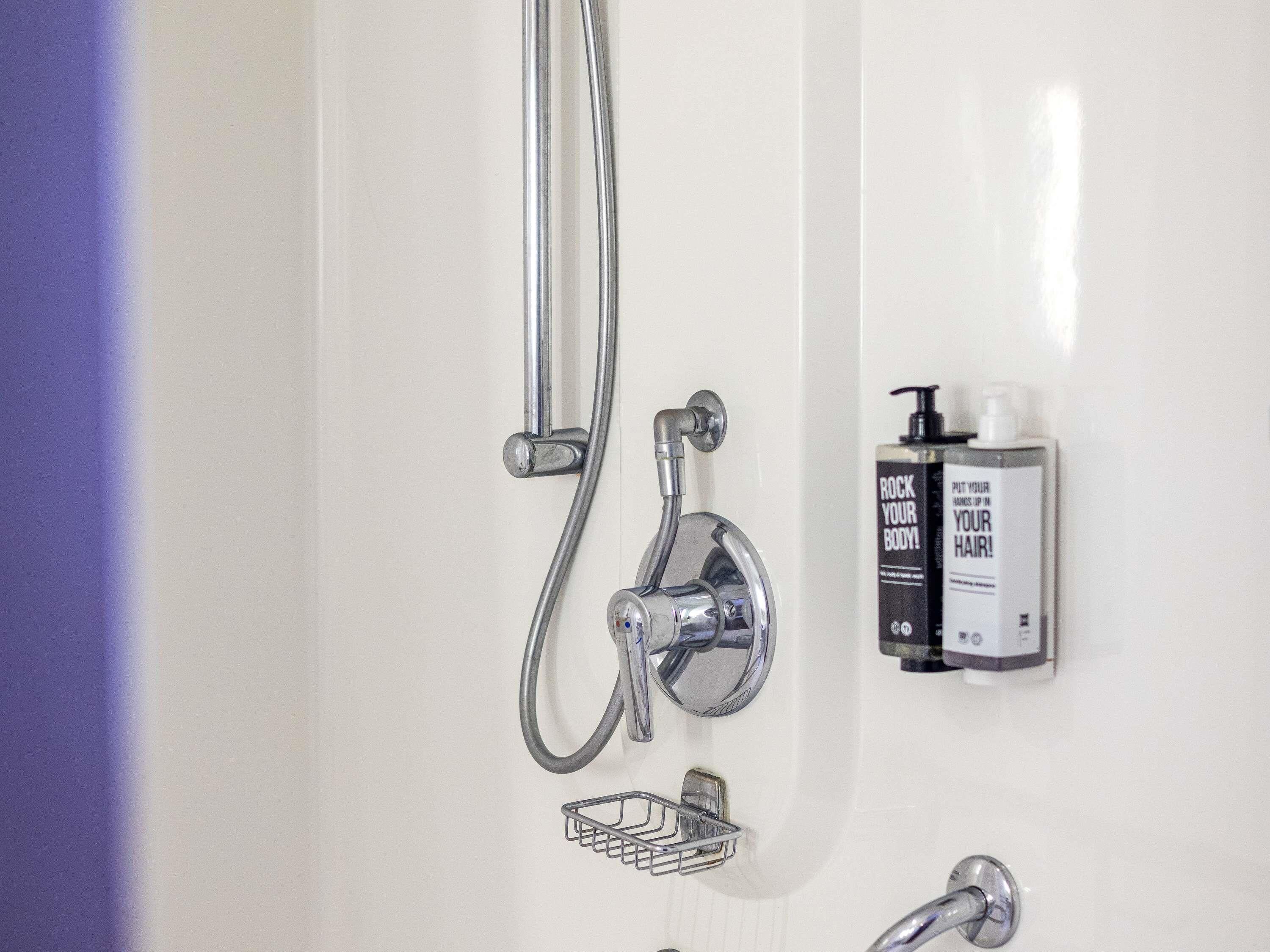 Un bagno con doccia, un erogatore di sapone e un piccolo cesto metallico.