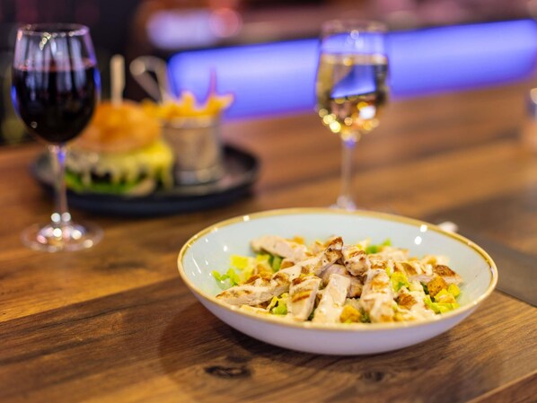 A dining table with a plate of food, two glasses of wine, and a blurred background.