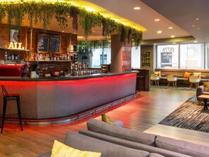A bar area with a red illuminated counter, seating with cushions, and hanging plants. - ibis London City - Shoreditch (London)