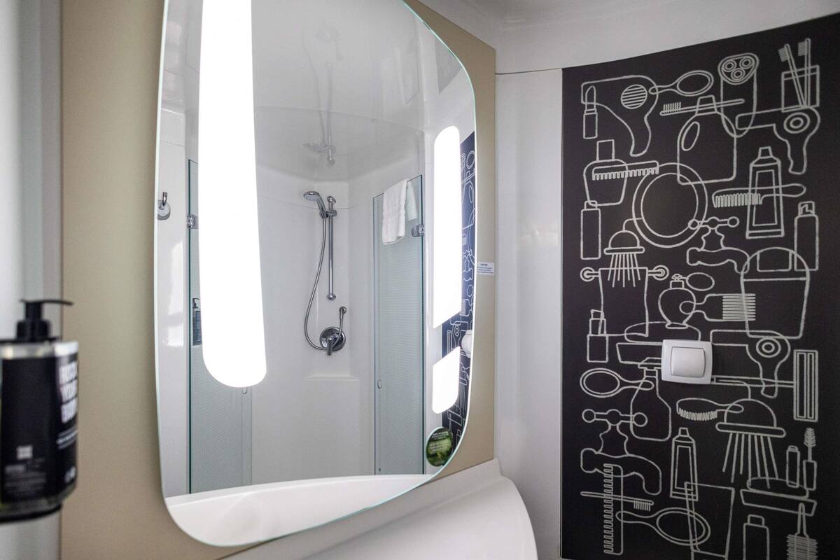 A bathroom with a large mirror, a shower, and a wall with bathroom-related icons.
