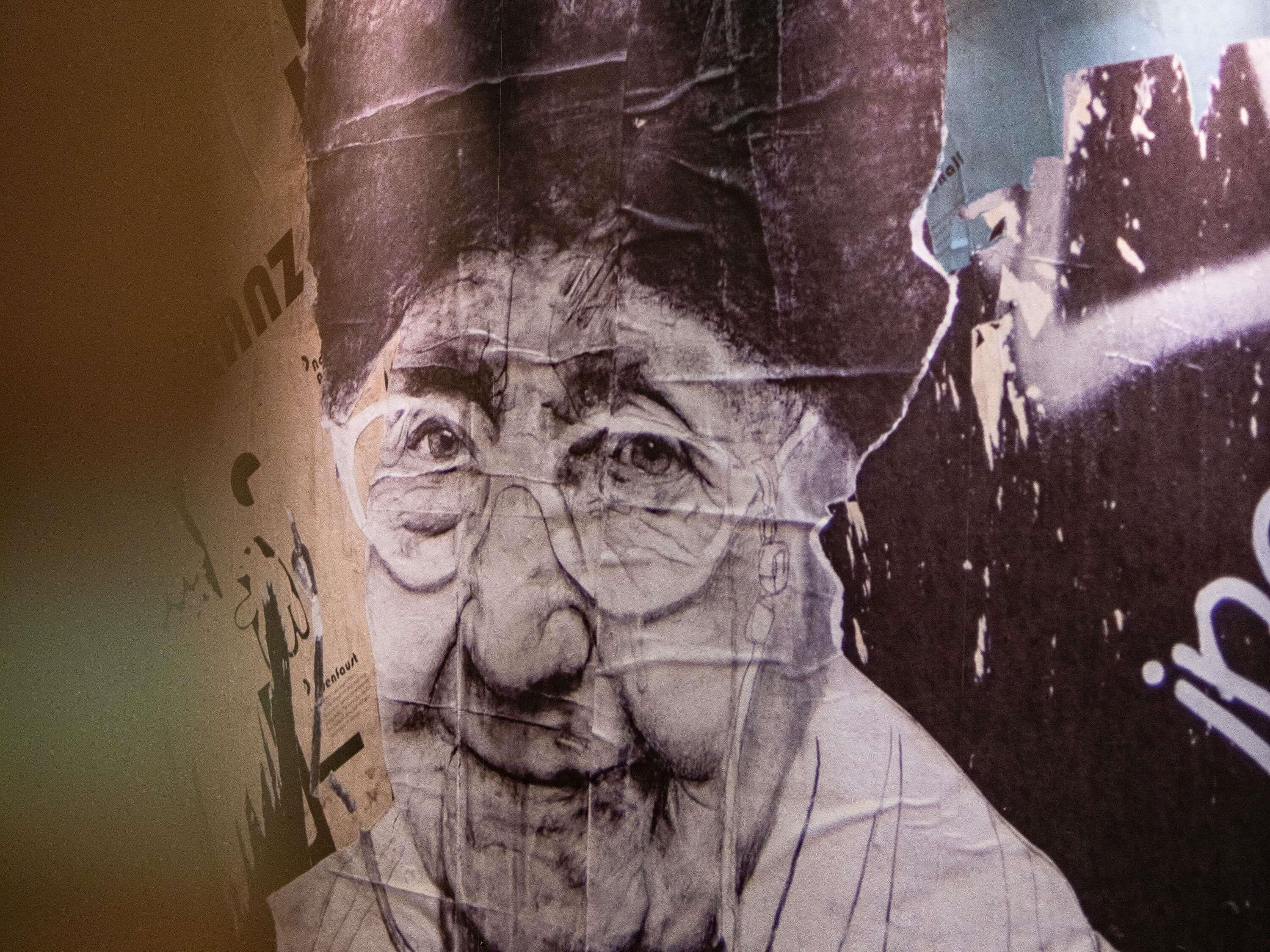 A wall with a large, torn poster featuring a person's face.