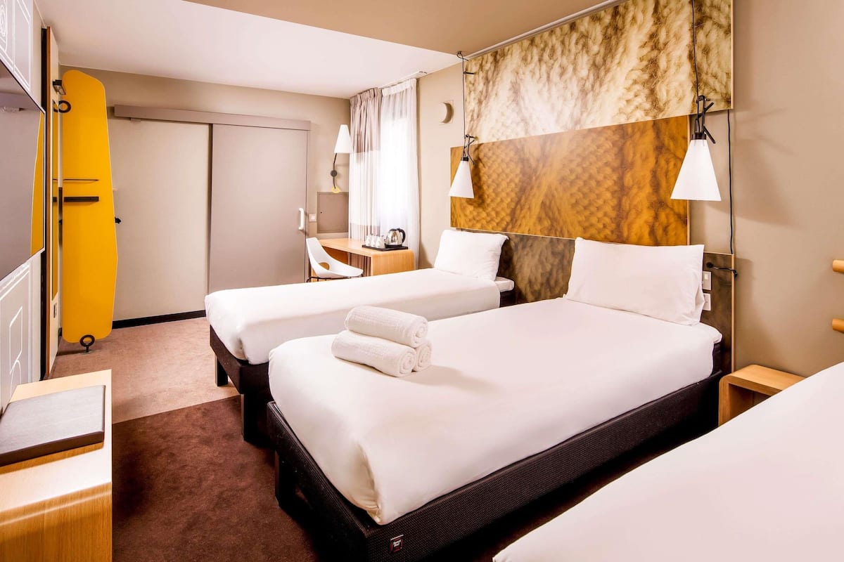 A hotel room with two beds, a desk, a chair, a surfboard, and a large wall mural.