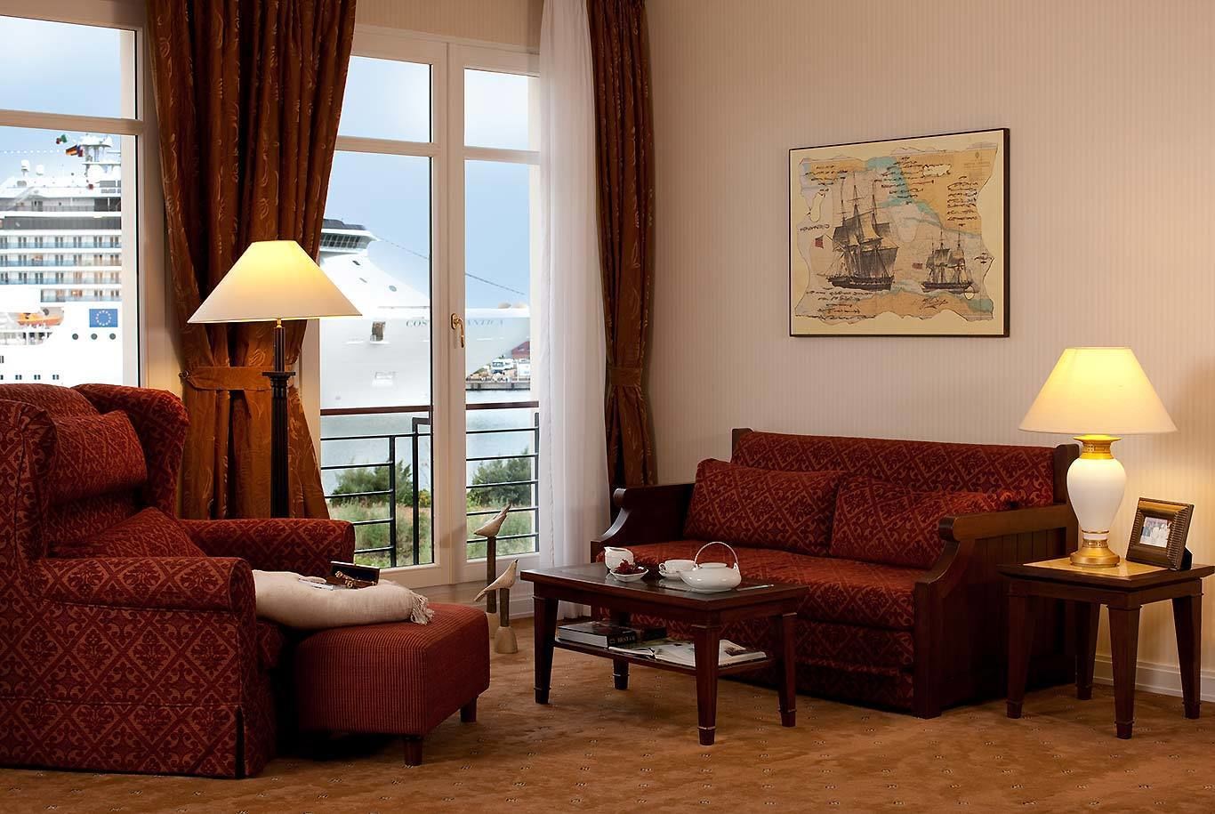 Una sala de estar con sofá, sillón y mesa de centro, un cuadro en la pared y vista a un crucero a través de una ventana.