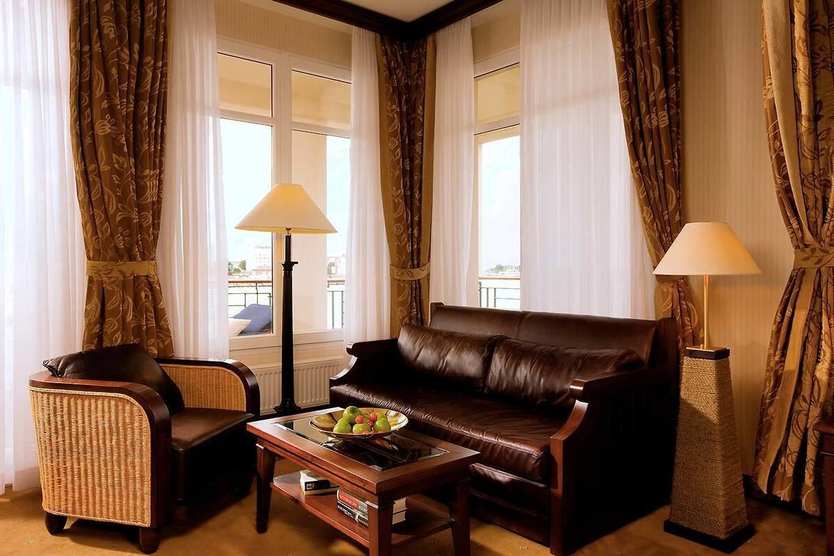 Ein Wohnzimmer mit einem braunen Ledersofa, einem Korbsessel, einem Couchtisch mit Obst und zwei Stehlampen.