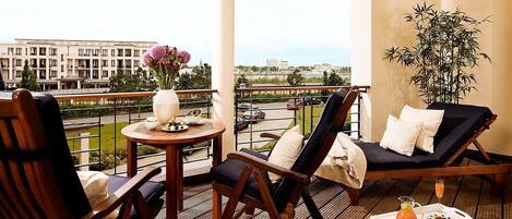 Een balkon met een houten tafel, twee stoelen, een lounge stoel en een bloempot.