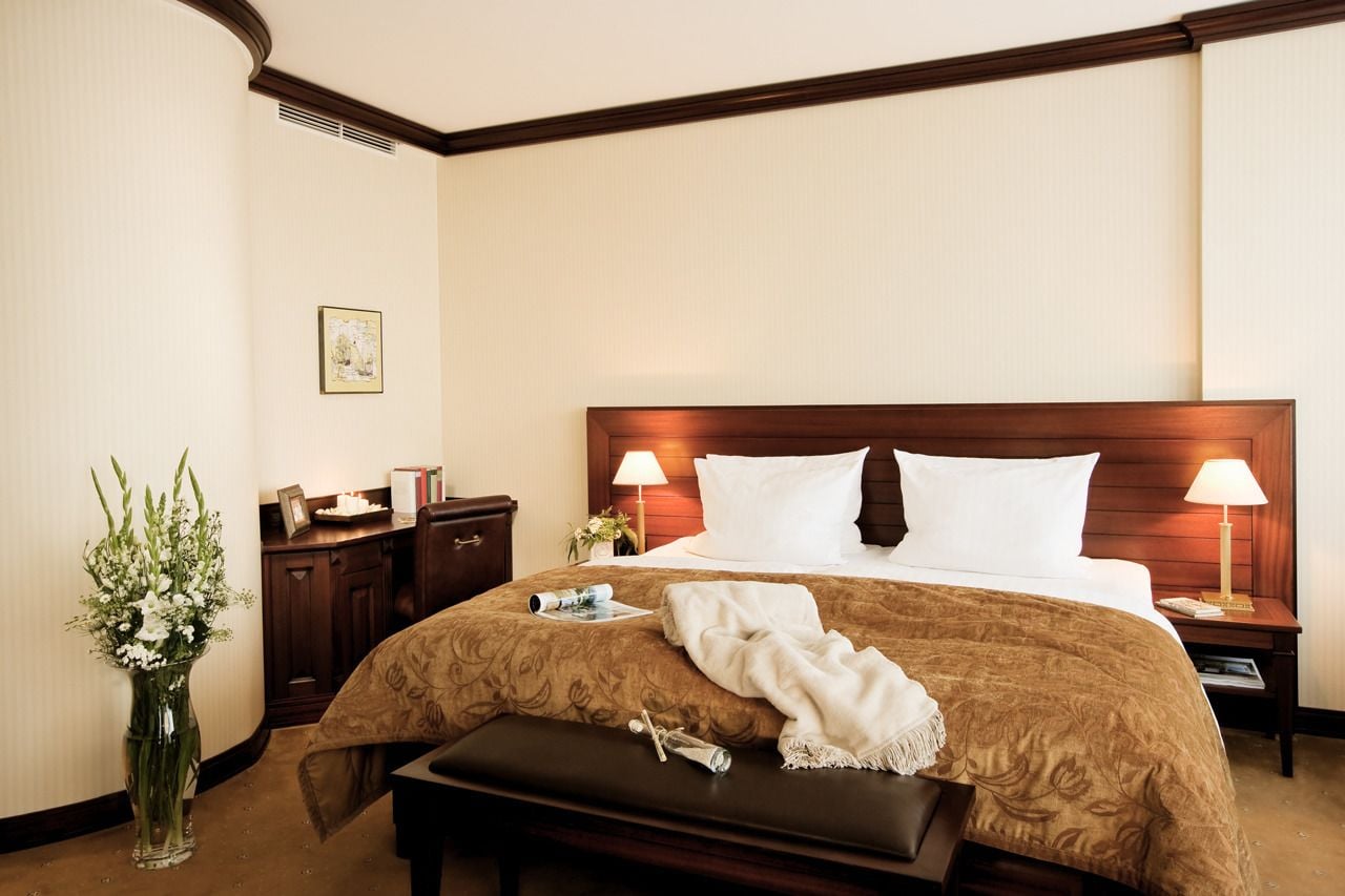 A hotel room with a large bed, two bedside tables, a nightstand, a vase with flowers, and a picture on the wall.