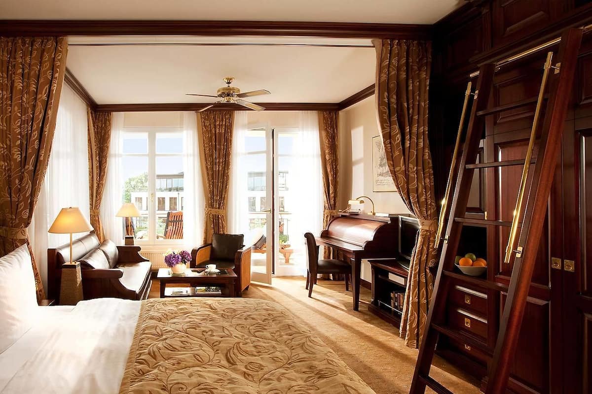 Ein Hotelzimmer mit Bett, Schreibtisch mit Klavier, Stuhl, Lampe und Blick ins Freie.