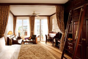 Habitación de hotel con cama, escritorio con un piano, silla, lámpara y vistas al exterior.