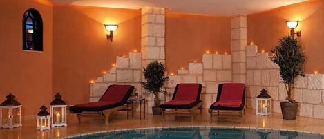 A pool area with three sun loungers, stone walls, and wall-mounted lights.