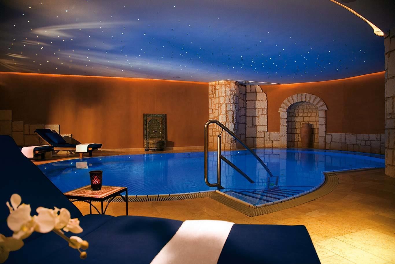 Une piscine intérieure avec un plafond étoilé, des chaises longues et un mur en pierre.